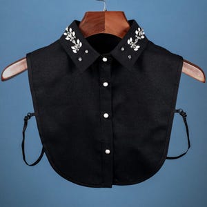 May include: A black faux collar with a button closure and a decorative rhinestone design. The collar is made of a soft, lightweight fabric and has adjustable straps.