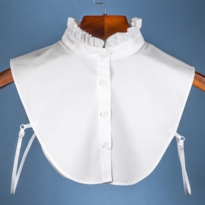 May include: White cotton detachable collar with a ruffled edge and button closure. The collar has two adjustable straps.