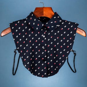 May include: A black faux collar with a white and red geometric pattern. The collar has two black straps that attach to the back of the neck.
