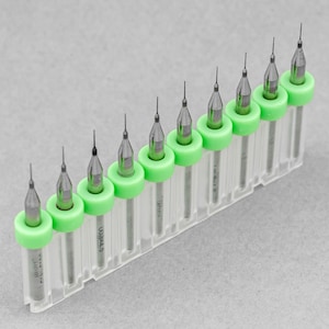 May include: A set of ten small drill bits in a clear plastic case with green caps. The drill bits are arranged in order of size, with the smallest bit on the left and the largest bit on the right.
