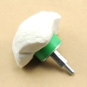 May include: A white cotton buffing wheel with a green plastic base and a silver metal shaft. The buffing wheel is attached to the base with a metal screw.