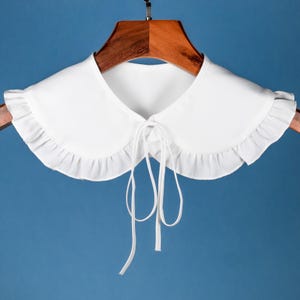 Puede incluir: Collar blanco con volantes y cierre de lazo. El collar está hecho de una tela suave y ligera, perfecto para agregar un toque de elegancia a cualquier atuendo.
