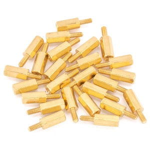 May include: A pile of gold-coloured metal standoffs, also known as spacers, for electronics projects. These standoffs are used to elevate circuit boards and other components.