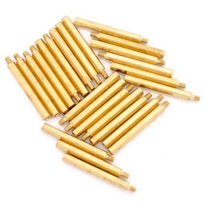 May include: A group of 20 gold-coloured metal standoffs, also known as spacers, are arranged in a pile on a white background. The standoffs are hexagonal in shape and have a smooth, polished finish.