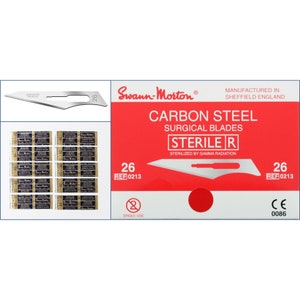 May include: A pack of sterile carbon steel surgical blades, size 26, manufactured by Swann-Morton in Sheffield, England. The pack is red and white with the text "STERILE R" and "REF 0213".