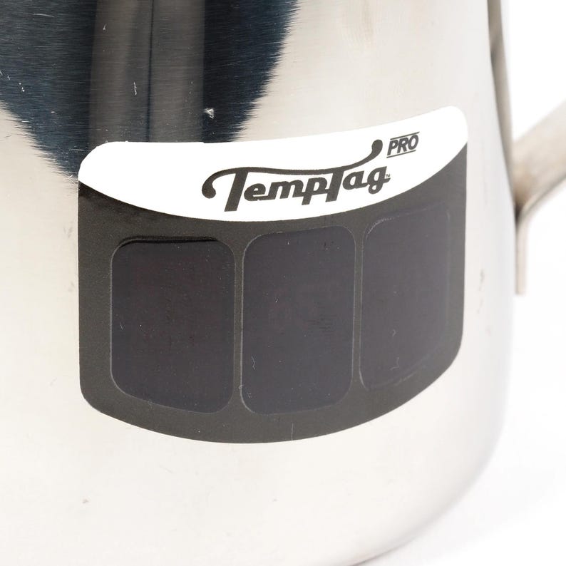 May include: A silver stainless steel pitcher with a TempTag PRO label. The label has three black rectangular areas that are likely for temperature readings.