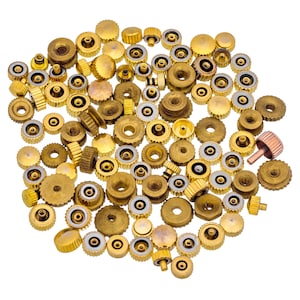 May include: A large collection of gold-toned metal watch crown parts. The parts are various sizes and shapes, with some having a raised edge and others having a flat surface.