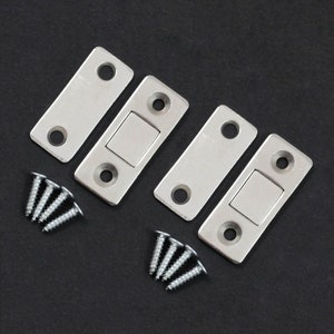 Può includere: Quattro fermagli magnetici per porte di armadio argentati con viti. I fermagli hanno una forma rettangolare con un piccolo magnete quadrato al centro.