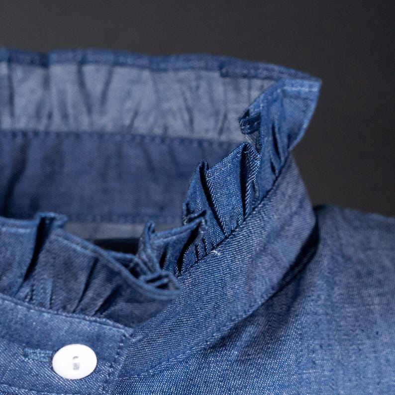 K&ouml;nnte beinhalten: Nahaufnahme eines Hemdkragen aus Jeans mit R&uuml;schenbesatz. Der Kragen ist dunkelblau und die R&uuml;schen sind in einem helleren Blauton gehalten.