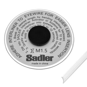 Pode incluir: Um disco branco e prateado com instruções para a inserção de lentes de óculos. O disco tem um centro preto e a marca "Sadler" impressa. Um fio de óculos branco está no canto inferior direito.