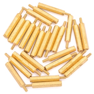 May include: A group of 20 gold-coloured metal standoffs, also known as spacers, are arranged in a circular pattern on a white background. The standoffs are hexagonal in shape and have a threaded hole on one end.