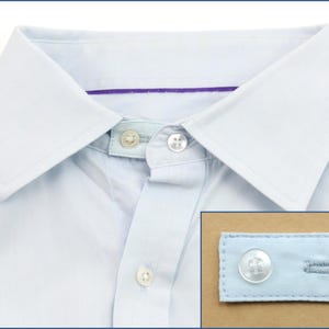 Könnte beinhalten: Ein hellblaues Hemd mit weißem Kragen und einem violetten Streifen auf der Innenseite des Kragens. Das Hemd hat zwei weiße Knöpfe vorne und einen weißen Knopf an der Manschette. Das Hemd ist aus einem weichen, bequemen Stoff gefertigt.