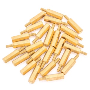May include: A pile of 20 gold-coloured metal standoffs, also known as spacers, for electronics projects. The standoffs are approximately 2.5 cm long and have a hexagonal shape.