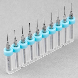 May include: A set of ten small drill bits in clear plastic cases with blue caps. The drill bits are arranged in order of size, with the smallest bit on the left and the largest bit on the right.