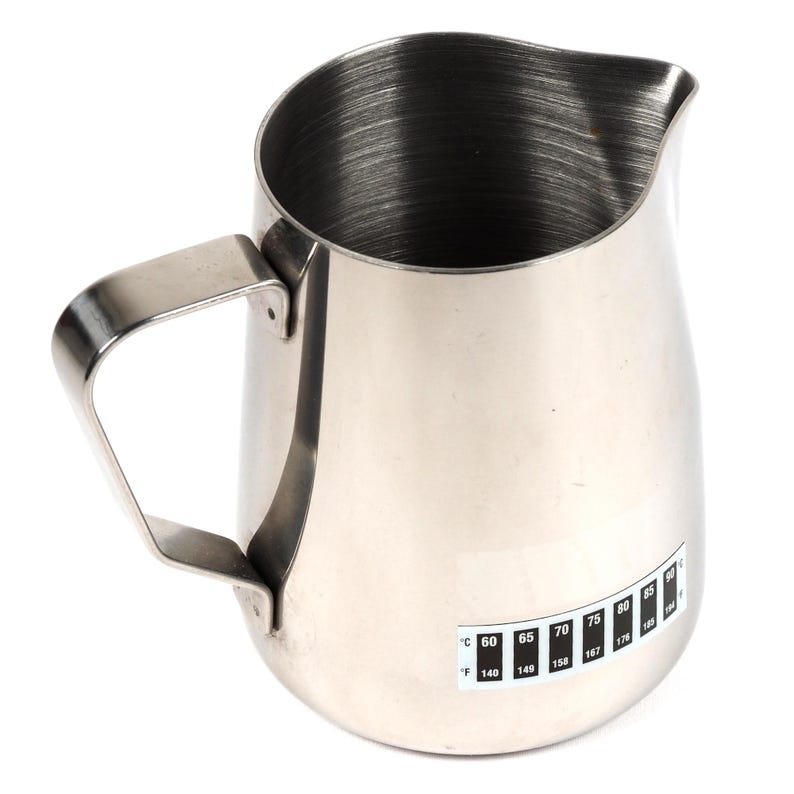 May include: A stainless steel milk frothing pitcher with a handle and a temperature scale in both Celsius and Fahrenheit. The scale ranges from 60 to 85 degrees Celsius and 140 to 185 degrees Fahrenheit.