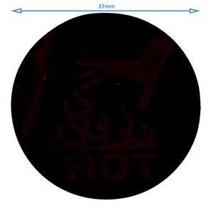 Op de afbeelding: Een zwarte, ronde waarschuwingssticker met een diameter van 37 mm, met een rode afbeelding van een hand boven vlammen en het woord "HOT" in het rood. De sticker is bedoeld om te waarschuwen voor een heet oppervlak.