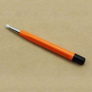 May include: A small, orange cleaning tool with a black handle and a white brush at the end. The tool is designed for cleaning small spaces and crevices.