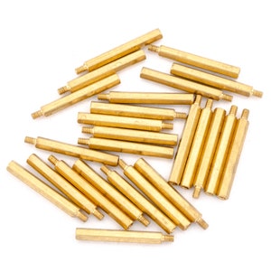 May include: A group of 20 gold-coloured metal standoffs, also known as spacers, are scattered on a white surface. The standoffs are hexagonal in shape and have a threaded end.