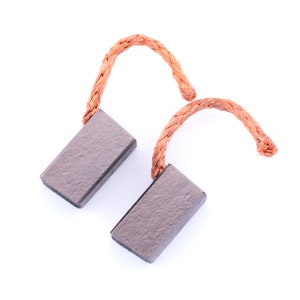 Pode incluir: Duas escovas de carvão cinzas com fios de cobre marrons. As escovas são retangulares e têm uma textura áspera.