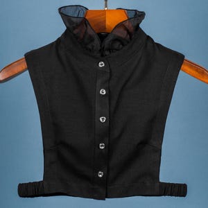 Peut inclure: Un faux col noir avec un volant en dentelle transparente. Le col a une fermeture boutonnée et est conçu pour être porté par-dessus une chemise ou un chemisier.