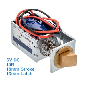 Könnte beinhalten: Ein silbernes und messingfarbenes Solenoid-Türschloss mit 6 V DC, 15 N, 10 mm Hub und 10 mm Riegel. Das Schloss hat rote und schwarze Drähte daran befestigt. Das Etikett auf dem Schloss lautet "TAU-0837DL 6VDC 10mm 1A 15N".