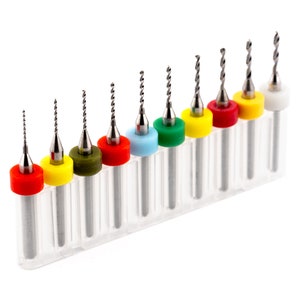 May include: A set of nine drill bits with silver shafts and spiral flutes. Each bit has a coloured collar: red, yellow, green, blue, and white. The bits are arranged in a clear plastic holder.