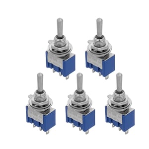 Peut inclure: Cinq interrupteurs à bascule argentés avec des bases en plastique bleu. Chaque interrupteur porte l'inscription "ON OFF ON" et "6A 125VAC" imprimée sur la base.