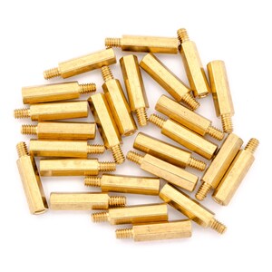 May include: A group of 20 gold-coloured metal standoffs. The standoffs are hexagonal in shape and have a threaded hole on each end.