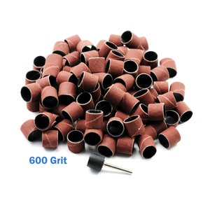 May include: A pile of 600 grit sanding drum sleeves for use with rotary tools. The sleeves are brown and have a black rubber backing. There is a single sanding drum sleeve attached to a metal mandrel.