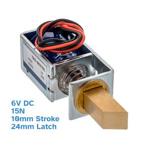 Könnte beinhalten: Ein silbernes und messingfarbenes magnetisches Türschloss mit roten und schwarzen Drähten. Das Schloss hat einen Hub von 10 mm und einen Riegel von 24 mm. Das Etikett auf dem Schloss lautet "TAU-0837DL 6VDC 10mm 15N".