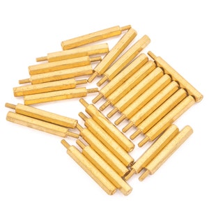 May include: A selection of brass standoffs, featuring a hexagonal body and threaded ends. The standoffs are displayed on a white background, highlighting their golden hue and consistent design. These components are typically used in electronics and hardware applications.