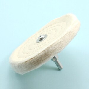 May include: A white cotton buffing wheel with a metal center screw and a threaded shaft. The wheel is designed for polishing and buffing metal surfaces.