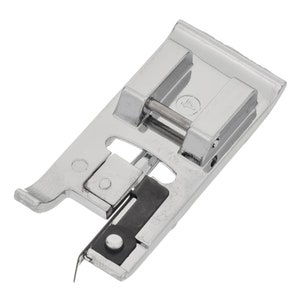 Pode incluir: Um calcador de máquina de costura brilhante, de cor prateada, com um pequeno componente preto. O calcador tem uma forma retangular com uma borda arredondada e um pequeno pino de metal. O número 4 está estampado na parte superior.