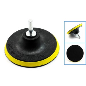 May include: A black sanding pad with a yellow outer ring and a silver shaft. The pad has the text "100 MM MAX 12000 RPM" printed on it.