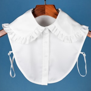 May include: A white detachable collar with a ruffled edge. The collar has a button closure and two ties.