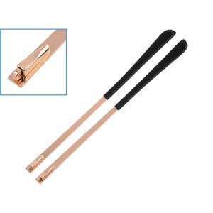 May include: A pair of rose gold metal eyeglass arms with black plastic tips. The arms have a spring hinge mechanism.