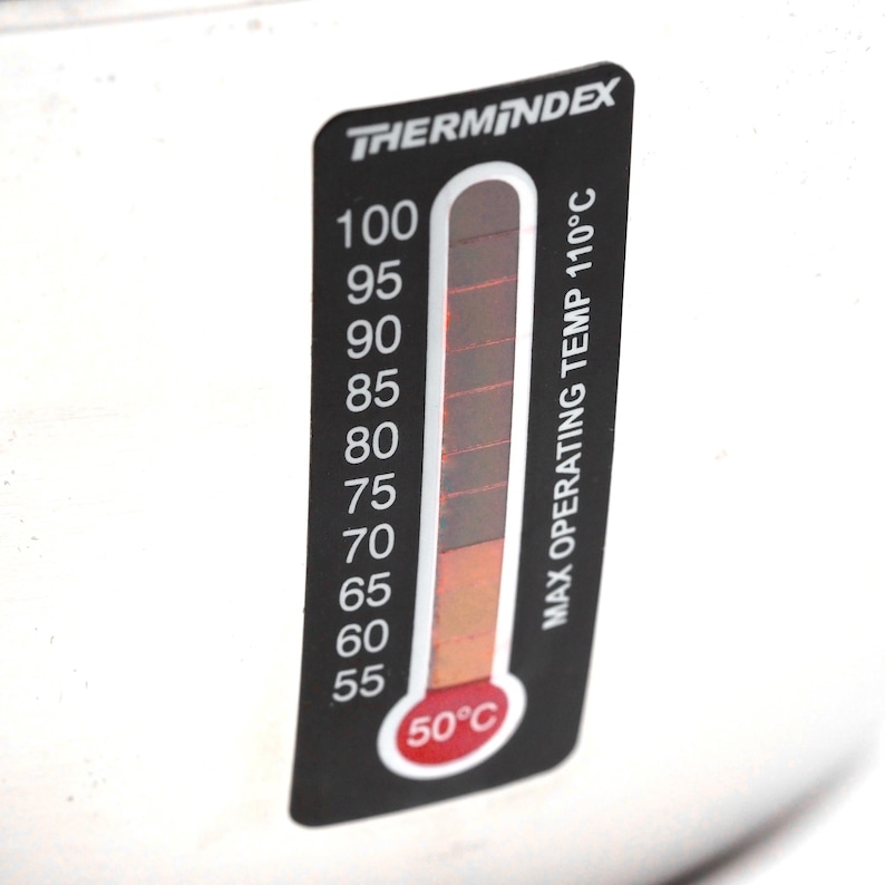May include: A black and white thermometer with a red needle indicating a temperature of 50 degrees Celsius. The thermometer has a black background with white markings and the text "THERMINDEX" and "MAX OPERATING TEMP 110&deg;C".