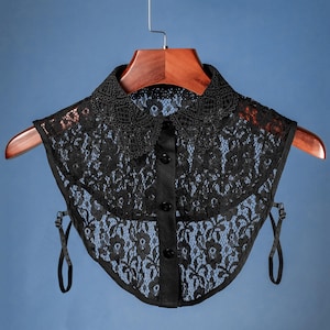 Puede incluir: Collar de encaje negro con cierre de botón. El collar está hecho de encaje delicado y tiene un borde festoneado.