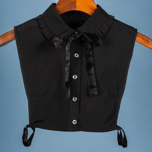 May include: A black faux-collar with a velvet bow tie. The collar has a ruffled edge and a button closure.