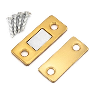 Op de afbeelding: Een gouden magnetische deurvanger met twee schroeven. De vanger heeft een rechthoekige vorm met een kleine, rechthoekige magneet in het midden. De vanger is ontworpen om een deur gesloten te houden.