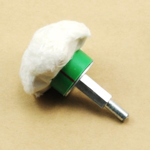 May include: A white buffing pad attached to a green and silver polishing tool. The tool has a threaded end for attaching to a drill or other power tool.