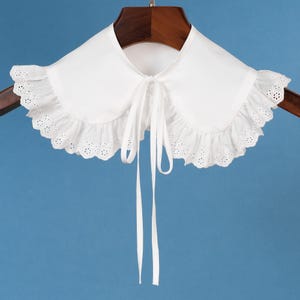 Puede incluir: Collar de encaje blanco con cierre de lazo. El collar tiene un borde festoneado y detalles de ojales.