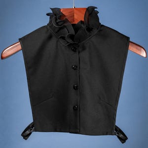 以下が含まれることがあります： フリルネックとボタン留めが特徴の黒いフェイクカラー。柔らかく軽量な生地で作られており、どんな服装にもエレガントさを添えるのに最適です。