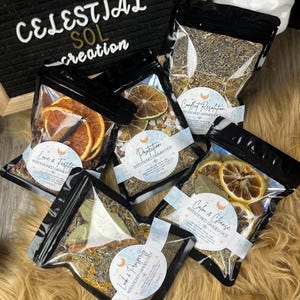 May include: Five small bags of dried herbs and fruit, labeled with the names of different intentions, such as "Love & Fertility", "Protection", "Calm & Cleanse", "Conflict Resolution", and "Luck & Prosperity". Each bag is labeled "Intentioned Simmer Pot".