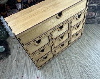May include: A wooden box with a lid and 10 small drawers. The drawers are all closed and have a light brown finish. The box is sitting on a wooden surface.