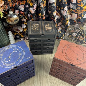 May include: Three wooden boxes with drawers, each featuring a different zodiac constellation design. The boxes are painted in blue, black, and brown with gold accents. The constellations are Scorpio, The Sun, and Aries.