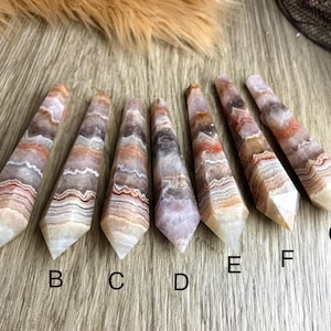 May include: Seven agate points with a layered, banded pattern in shades of white, pink, and brown. The points are arranged in a row from left to right, labeled A through G.