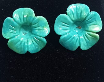 May include: A pair of turquoise flower-shaped earrings. The earrings are carved from turquoise and have a smooth, polished finish.