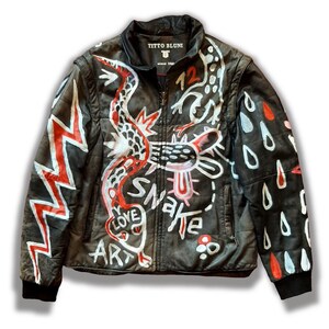 Puede incluir: Chaqueta de cuero negra con un dise&ntilde;o de serpiente blanca y roja, las palabras "Love Art Snake" y un rayo en el lado izquierdo, y gotas de lluvia blancas y rojas en el lado derecho. La chaqueta tiene una cremallera y una etiqueta que dice "Titto Bluni Since 1980".