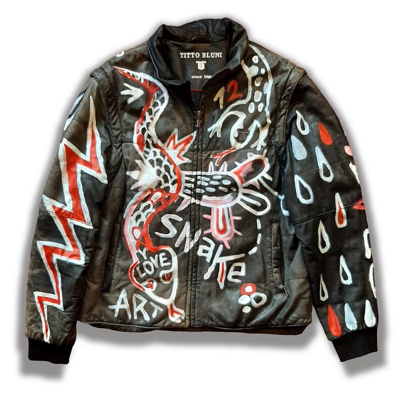 Puede incluir: Chaqueta de cuero negra con un dise&ntilde;o de serpiente blanca y roja, las palabras "Love Art Snake" y un rayo en el lado izquierdo, y gotas de lluvia blancas y rojas en el lado derecho. La chaqueta tiene una cremallera y una etiqueta que dice "Titto Bluni Since 1980".